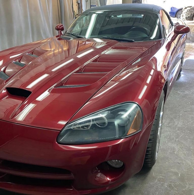 Red sports car with racing stripes parked in a garage, showing hood and front headlight detail